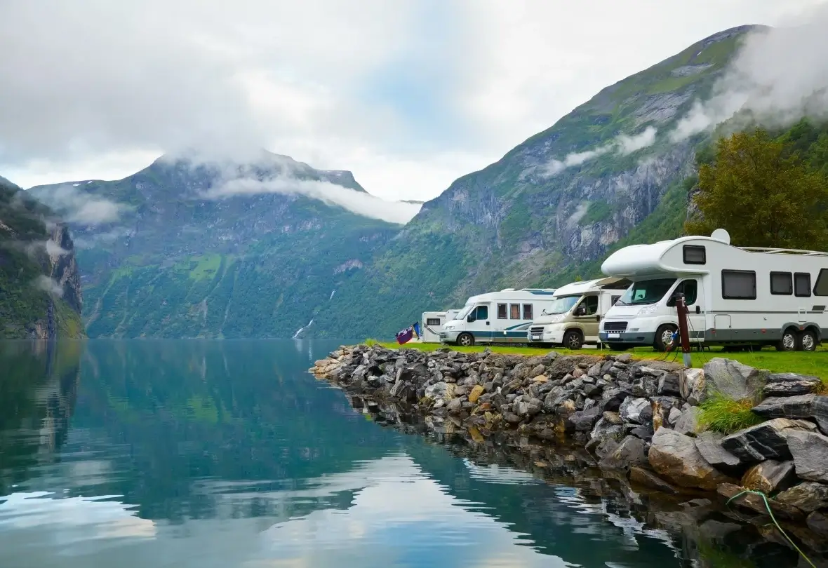 Several motorhomes parked near each at a designated dispersed camping area by a lake in the mountains.