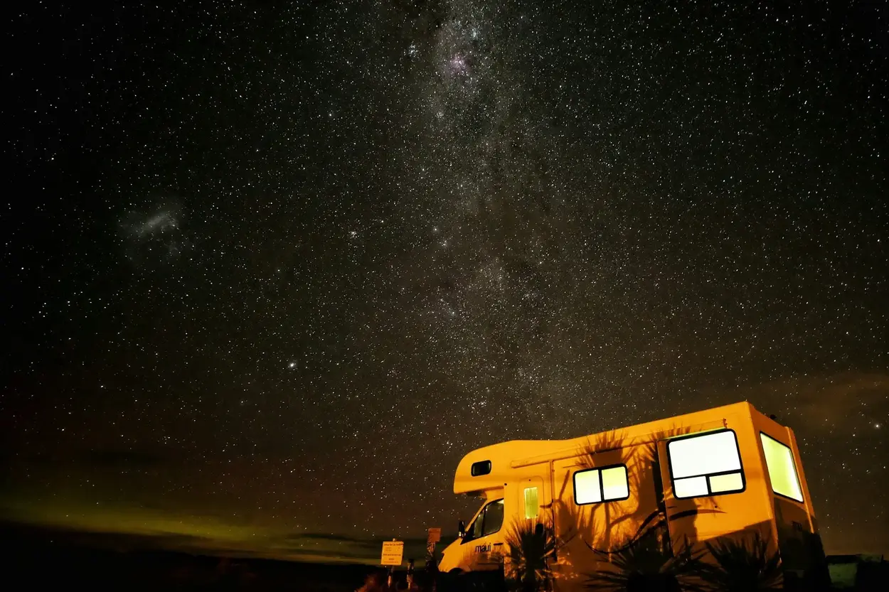 A Class C RV boondocking in an open area at night under a starry sky.
