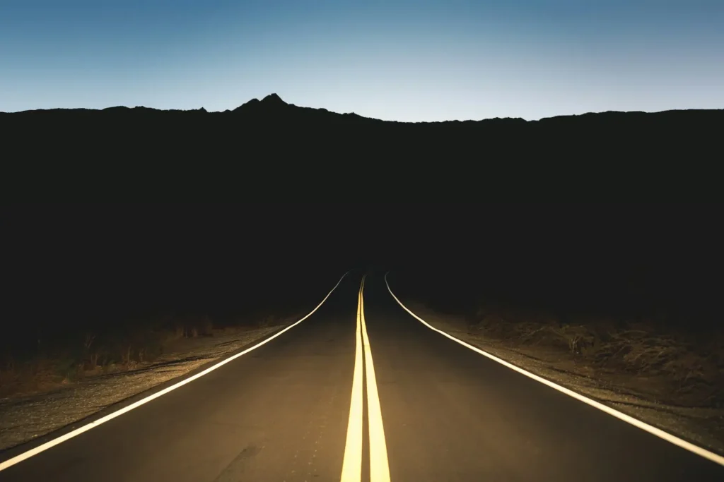 A long, dark road in Califonria at night with only the headlights illuminating ahead.