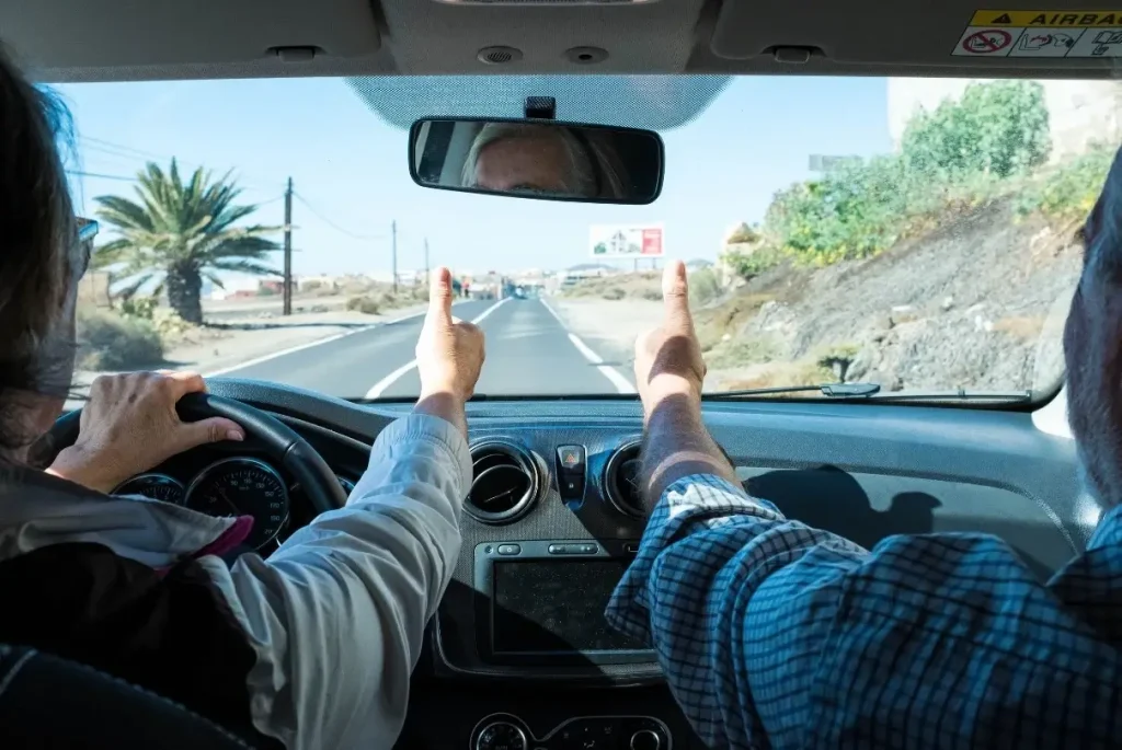 Two happy campers on a road trip giving a thumbs up at the windshield after establishing what is boondocking and stocking for some off-grid adventures.