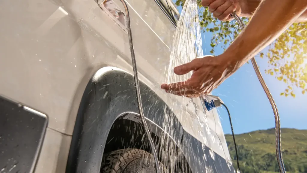 An RVer using an outdoor handheld camping shower outside their motorhome after installing one of the best RV water pumps out there.