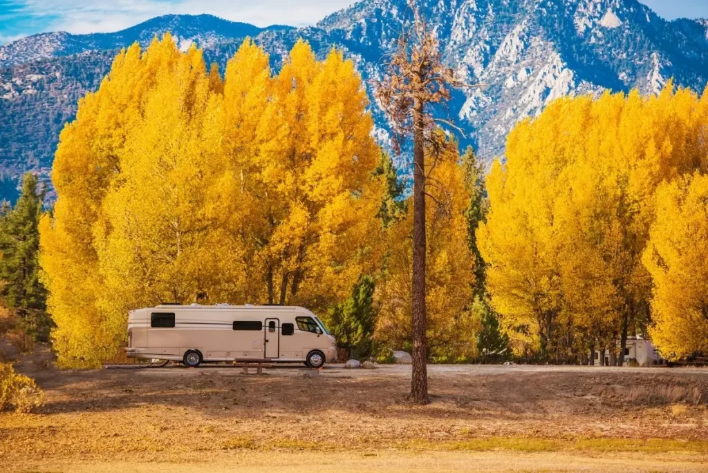 A motorhome parked in a dispersed camping RV campground in California backed by a scenic fall tree and mountain line.