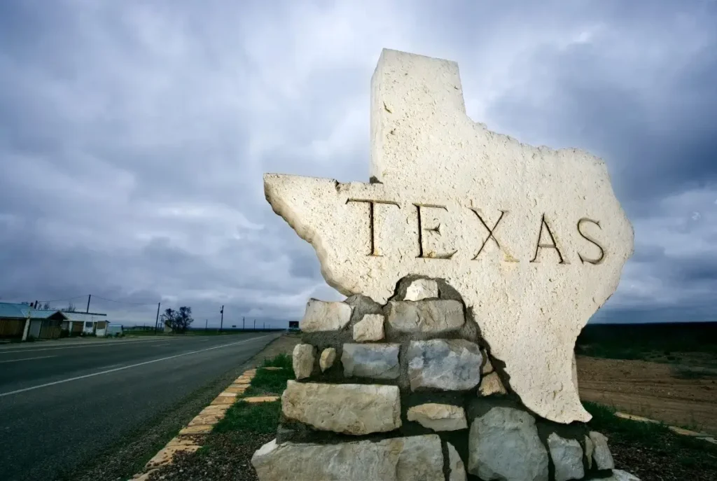 A Texas sign at the border shaped like the state itself on a moody, overcast day.