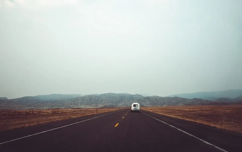 An old camper-style RV drives down a long, flat, misty road in the wilderness of Wyoming