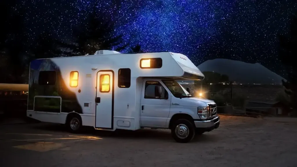 A Class C motorhome camped under a night sky with the windows illuminated and warm from using one of the best RV space heaters inside.