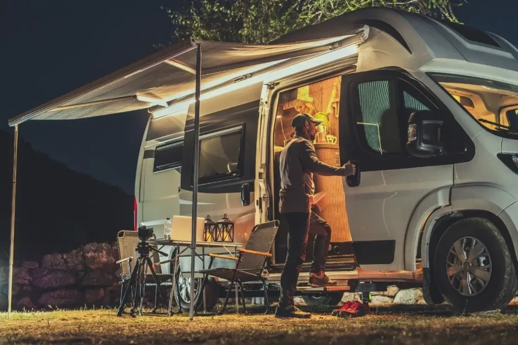 A man enters his Class B motorhome at night that is illuminated by a collection of the top gadgets for RVing.