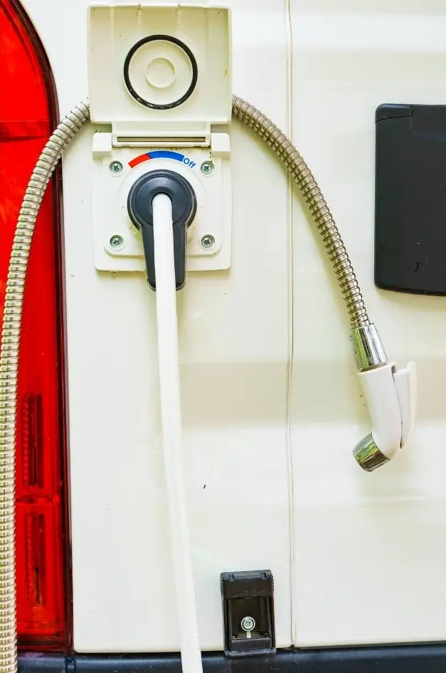 An outdoor shower hooked into the side of an RV's exterior with manual hot and cold settings for water temperature.