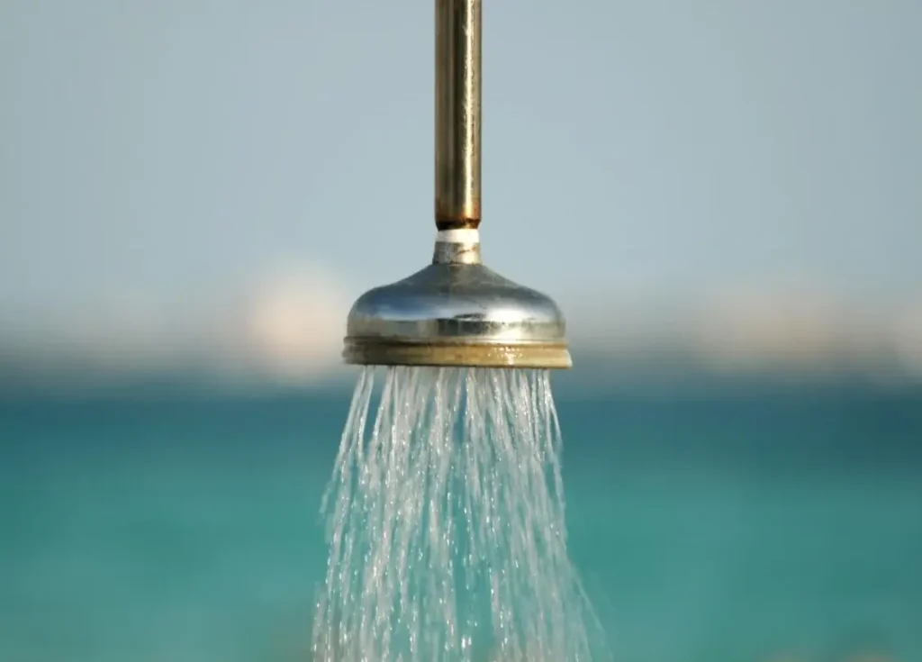 A hot outdoor shower powered by tankless RV water heater in operation at a waterside camp.
