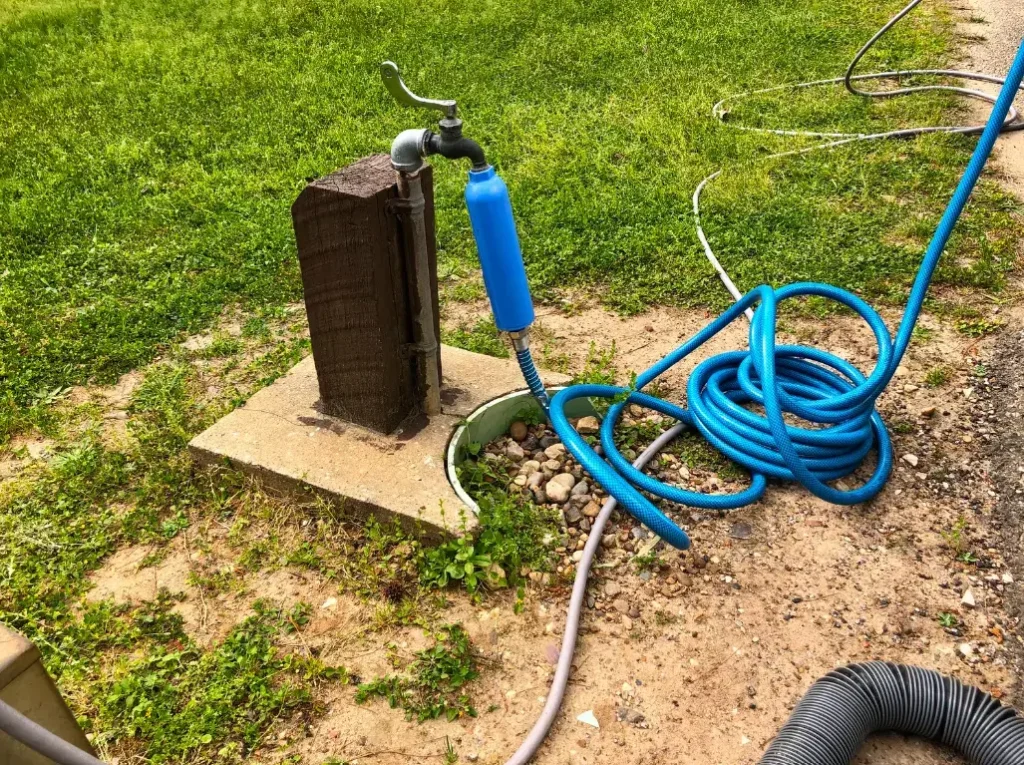 One of the best RV water hoses from our list hooked-up to a water fixture and motrohome in a developed campground.