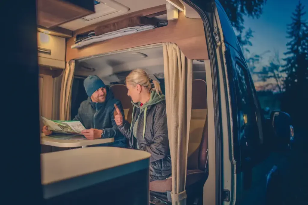 A traveling couple sitting inside their illuminated motorhome at night, trip-planning while powering their camp with one of the best RV inverter chargers.