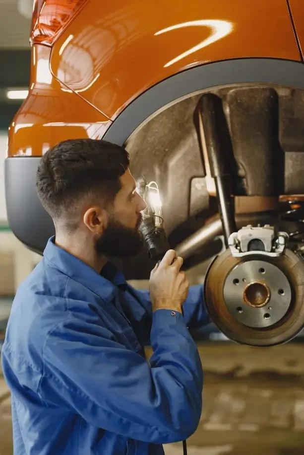 A mechanic diagnosing the cause of a hoisted RV's mechanical breakdown in his workshop.