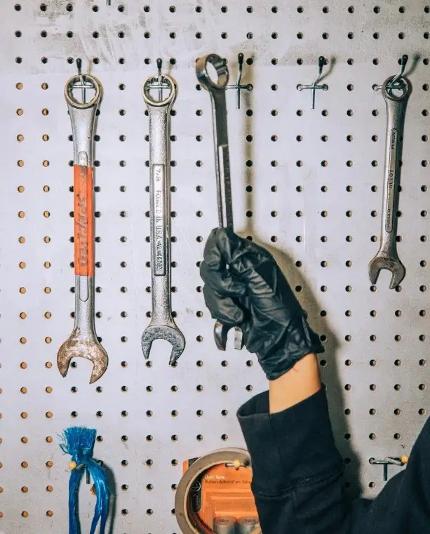An RV mechanic's hand in the workshop taking a wrench down from an array of hanging repairs and maintenance tools.