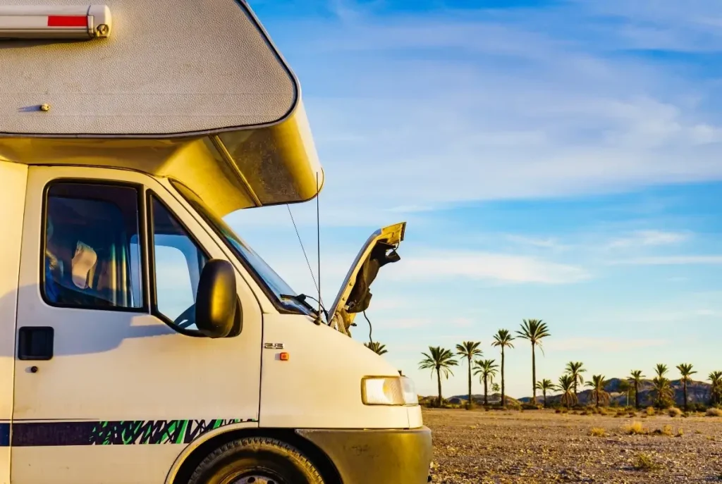 An RV experiencing mechanical issues in the desert with its hood popped for repairs.