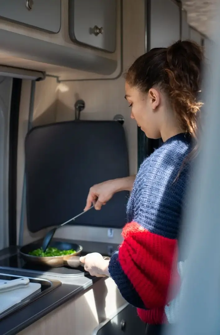 A woman cooking an easy RV meal of scrambled eggs and spinach on her motorhome's built-in stove.