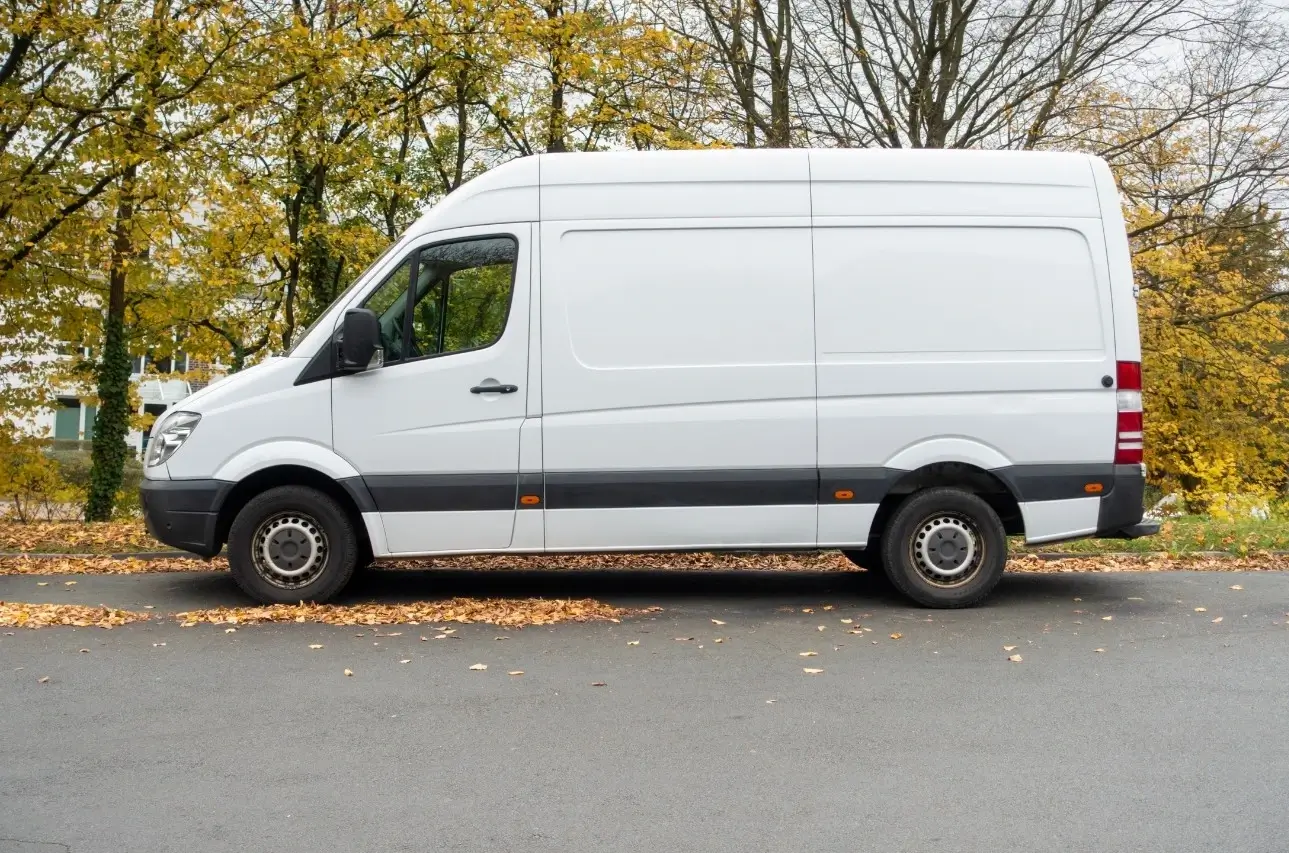A Ford Transit, our pick for the best overall van for a camper conversion project, parked on a street surrounded by colorful orange and yellow trees.
