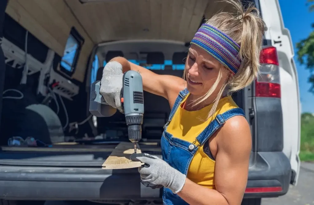 A woman works on her camper van conversion process, using a drill to make modifications to the empty vehicle's spacious interior.
.