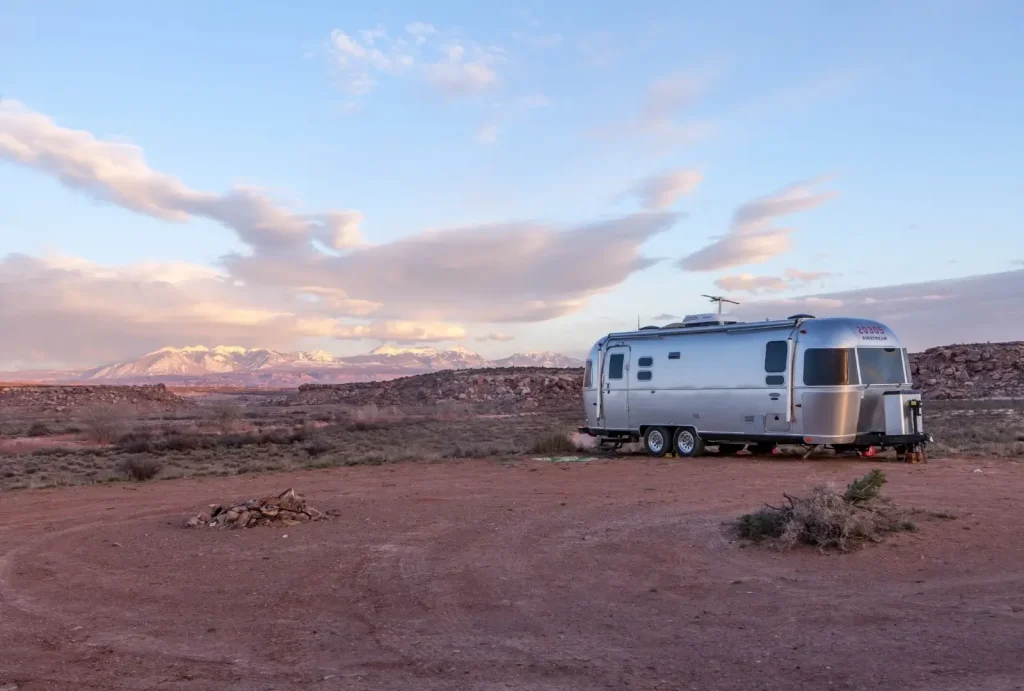 An Airstream travel trailer, best known for its quality, is parked in the desert with mountains and clouds in the background.