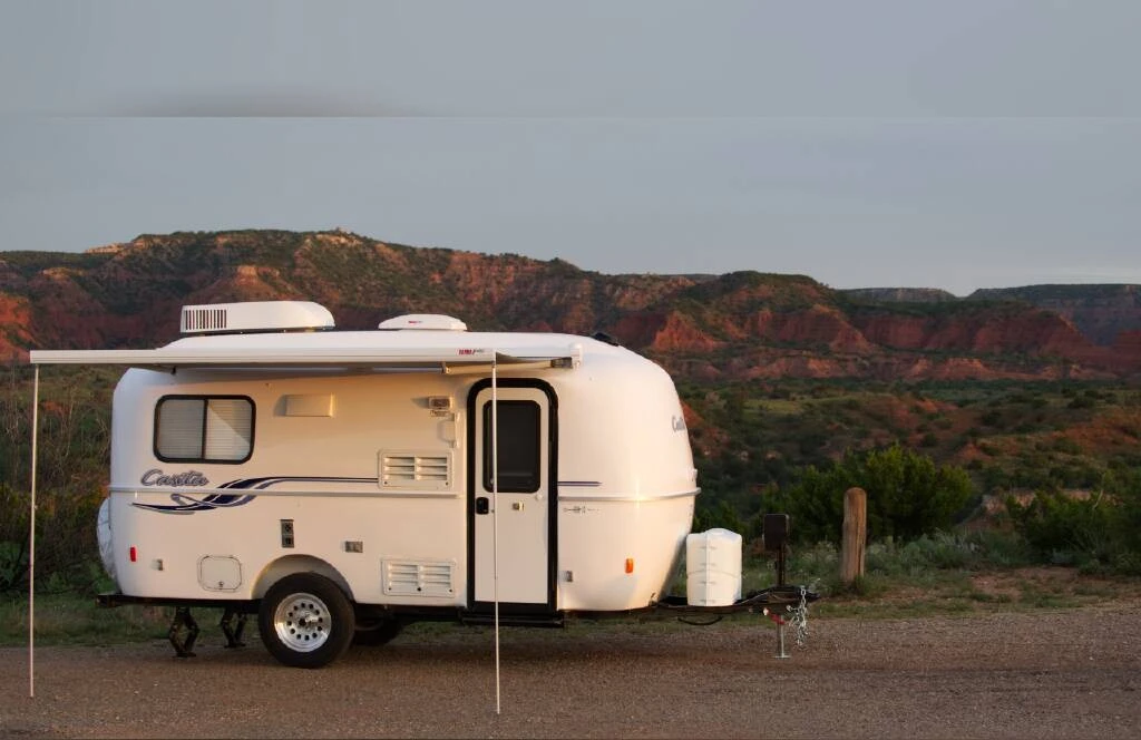 In the foreground of a mountainous terrain, a white fiberglass Casita travel trailer is parked with its awning extended.