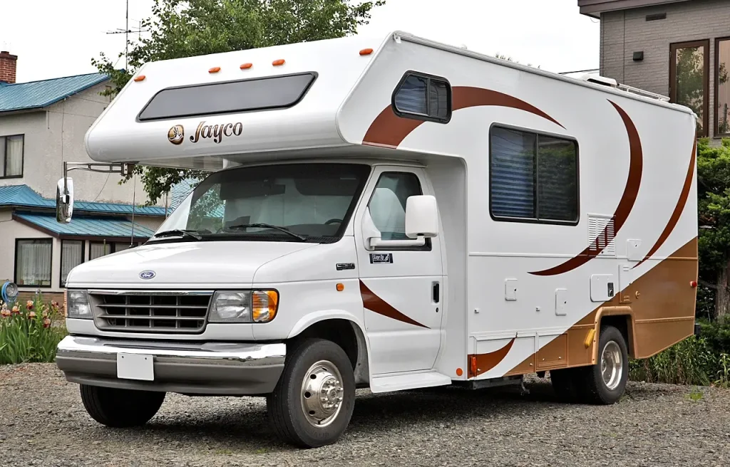 A Jayco Class C motorhome is parked on the gravel driveway of a home.