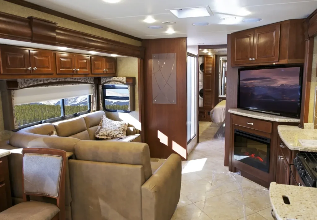 The living room of a Class A motorhome, featuring a TV, sofa, and real wood cabinetry, showcases high-quality materials.