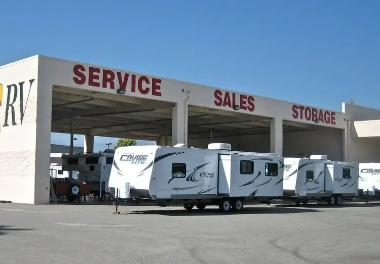 Travel trailers parked in front of an RV dealers garage offering service, sales, and storage of motorhomes.