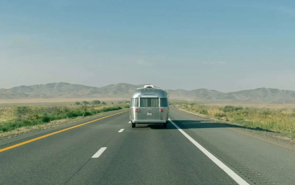 An old-school RV driving down the road with mountains in the background after being dewinterized.