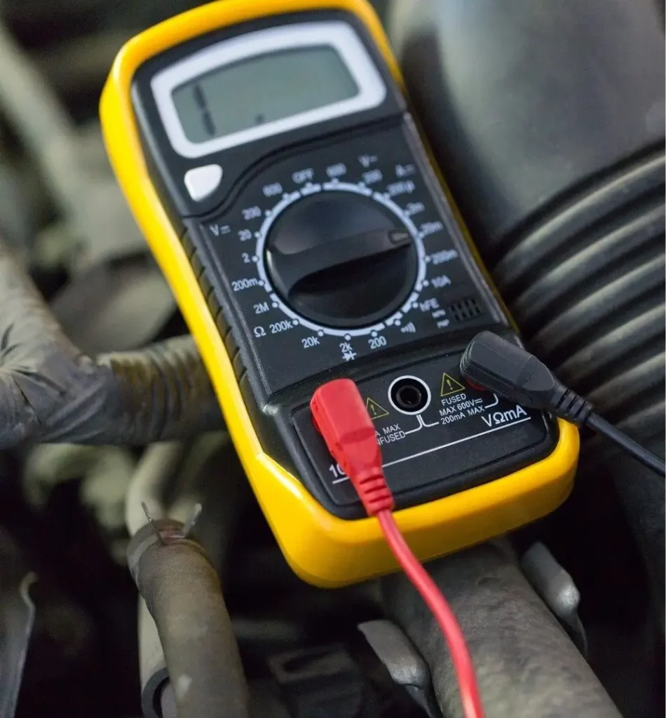 A multimeter placed on an engine block, measuring the RV's internal battery voltage during dewinterization processes.