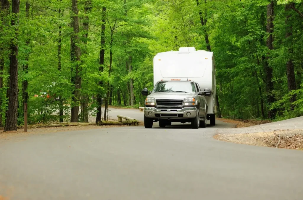 A pickup truck struggles to tow a fifth wheel up a steep hill on the road through the woods.