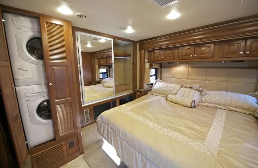 A luxurious fifth wheel RV bedroom with a king-sized bed and a washer and dryer illustrates some of the comforts of home.