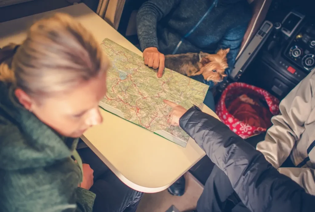 A family and their dog sit at the kitchen table in their pop-up camper, pointing to places on a map.