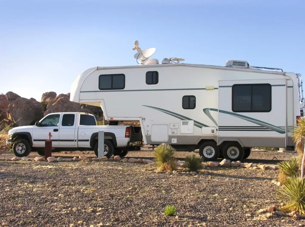 A shorter-than-average white fifth wheel, hitched to a white pickup truck, set in a desert with rock formations in the background.