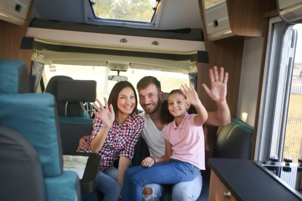 A family of three inside their camper van excitedly waves at the camera after making a sale.