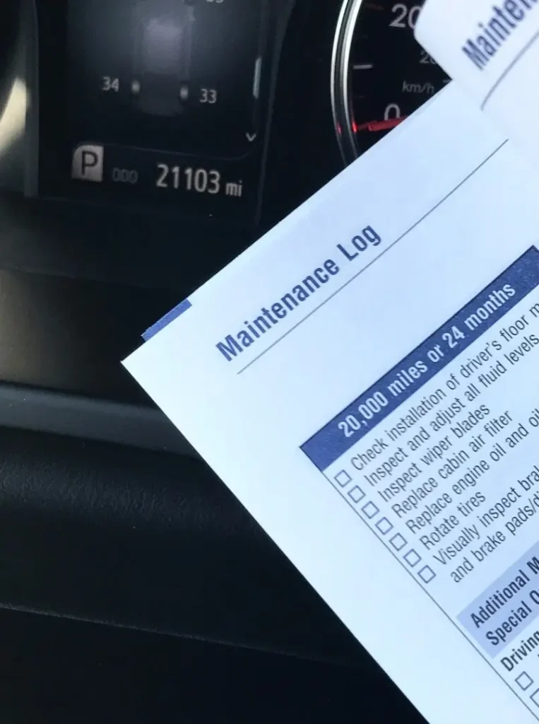 An RV's maintenance log is being reviewed from the driver's seat, with the odometer in the background.