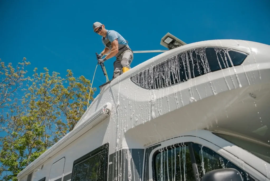 A man preparing his RV for sale and washing the roof of a Class C motorhome, with suds running down the sides and windows.