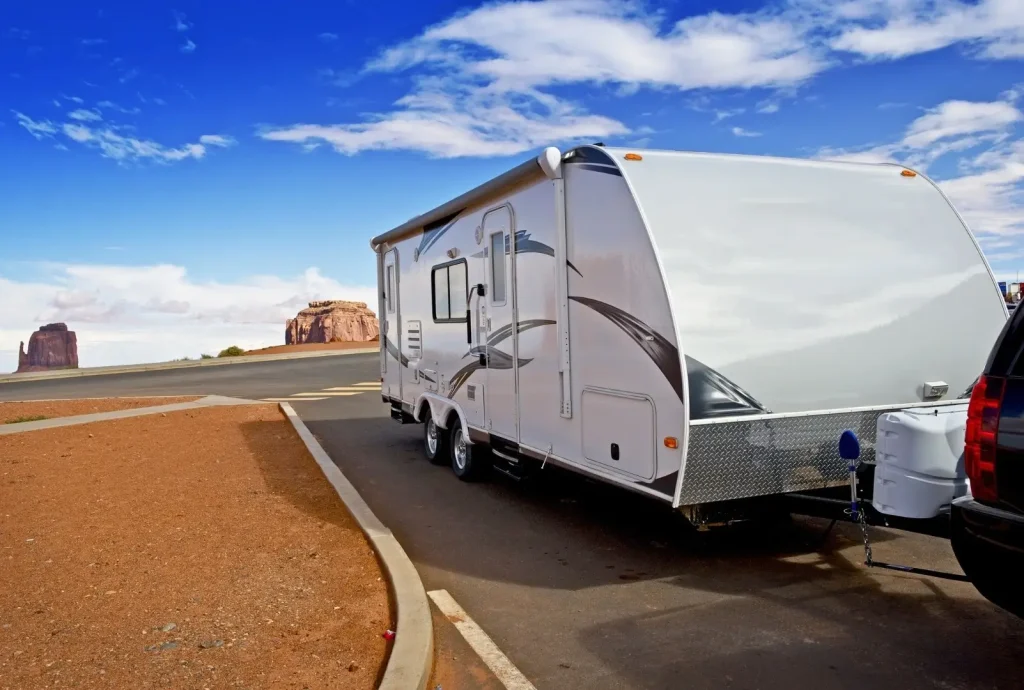 A very clean travel trailer hooked up to the tow vehicle, parked in front of rock formations under a blue sky.