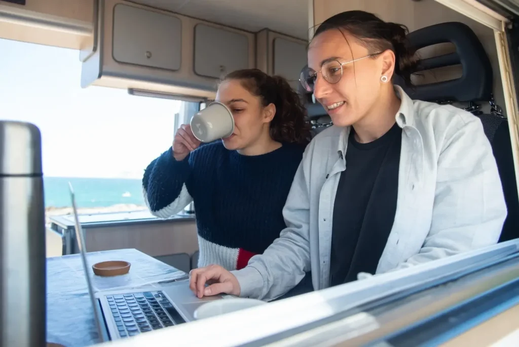 Two women in their motorhome by the ocean browse various listings online to help them determine how to price their RV for sale.