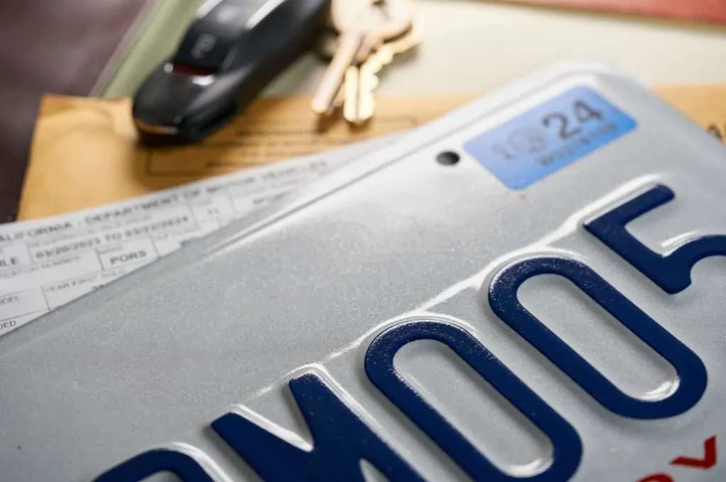 A license plate, pile of registration paperwork, and a set of keys on a desk, serving as a reminder of the essential documents needed to sell an RV.
